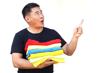 Handsome Asian man hold folded colorful clothes, point finger up with funny face expression. Excited.White background. Concept, daily chore, household. Folded clothes for neat and clean. Keep garment.