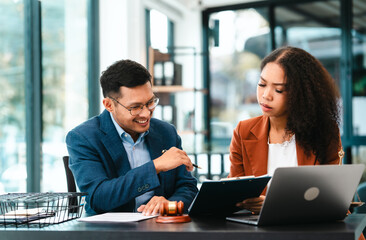 Attractive Asian businessman and an African American businesswoman, both in formal suits, intently review a contract paper together.