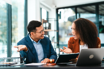 Attractive Asian businessman and an African American businesswoman, both in formal suits, intently review a contract paper together.