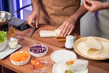 Obraz na płótnie Canvas Cropped view of chef influencers presenting fresh salad roll on cooking step by step, streaming via smartphone on social media live channel, showing ingredients vegetable soft tortilla wrap. Sellable.