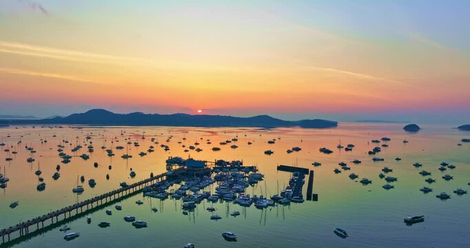aerial view yellow sunrise above Chalong pier..4K vdo of Majestic sunrise landscape Amazing light of nature cloudscape sky above mountain range. . boats yacht in Chalong marina gulf background.