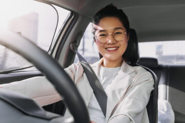 Asian Thai woman wearing glasses, happy smiling and looking camera while driving a car go to work in morning time.