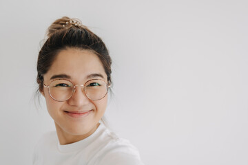 Happy asian Thai woman wear eye glasses with bun hair, taking selfie and smiling looking at camera, isolated over white background wall.