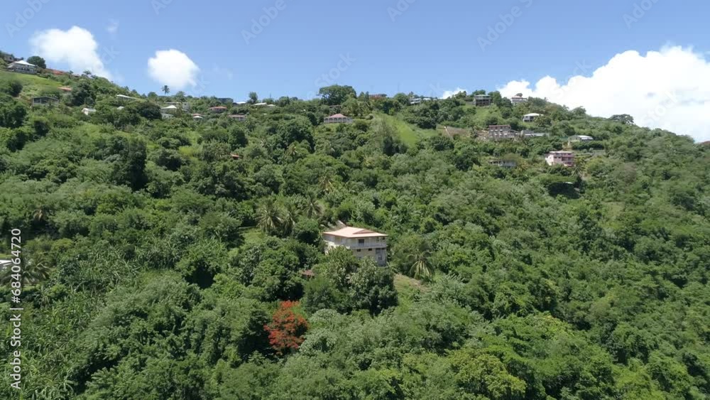 Sticker Drone shot around a forested hill with houses under a suny sky