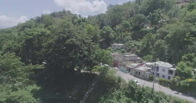 Drone shot around a forested hill with houses under a suny sky