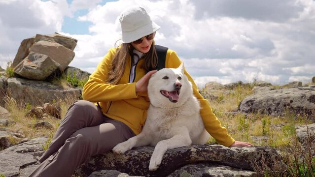 Happy young hiker woman cares and strokes lovely dog sitting on wild rocky area outdoors. Travel with friend pet, recreational lifestyle and tourism together with animals