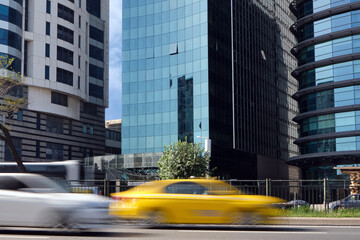 Yellow taxi drive quickly along the road in the city against the backdrop of skyscrapers.