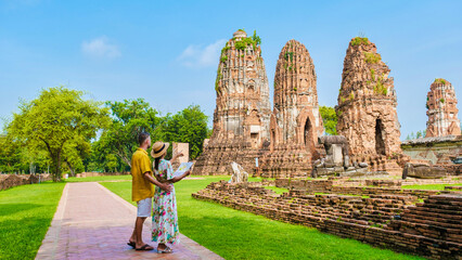 Ayutthaya, Thailand at Wat Mahathat, a couple of men and women with a hat and tourist map visiting Ayutthaya Thailand. Tourists with a map looking at a old temple in Thailand - obrazy, fototapety, plakaty
