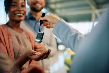 Close up of saleswoman giving car keys to her customer in showroom.