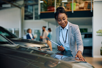 Happy black car saleswoman working in showroom.