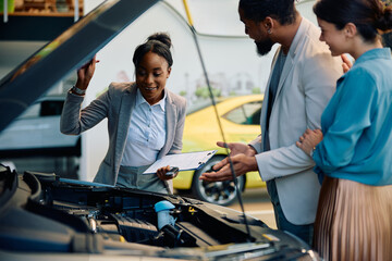 Happy black saleswoman selling new car to her customers in showroom.