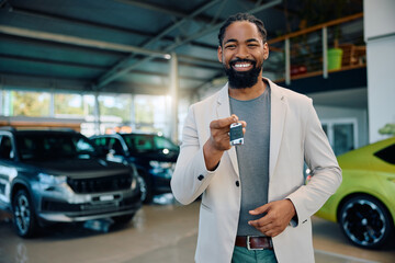 Happy black man holding his new car keys in showroom and looking at camera.