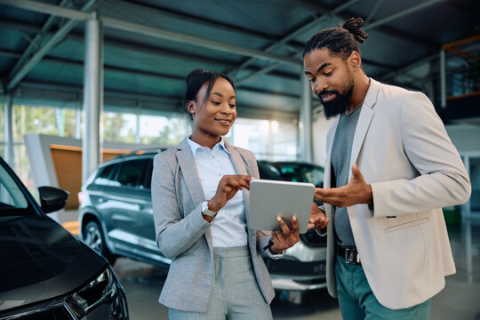 Black man and car saleswoman woman using digital tablet in showroom.