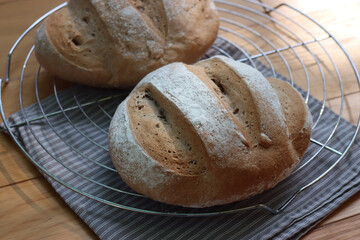 Homemade two wholegrain breads on a cooling rack on wooden table with gray napkin 