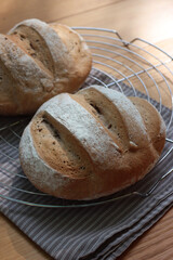 Homemade two wholegrain breads on a cooling rack on wooden table with gray napkin 