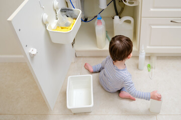 A child is playing with chemical cleaning products under the sink in the kitchen. Baby holds...