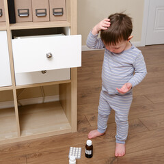 Toddler baby opened the cabinet drawer with pills and medicine. Child boy holding a pack of pills...