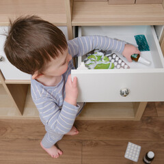 Toddler baby opened a cabinet drawer with pills and a vial of potion. Child boy holding medicine...