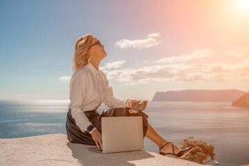 Freelance women sea working on a computer. Pretty middle aged woman with computer and phone outdoors with beautiful sea view. The concept of remote work.