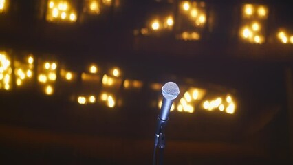 Single microphone on empty stage in large vintage concert hall with ceiling glowing with warm light. Event kickoff intrigue anticipation concept, low angle shot