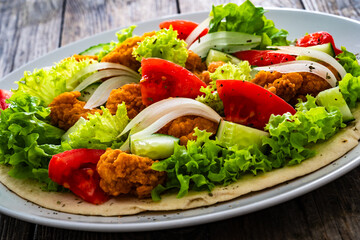 Seared chicken nuggets with vegetable salad on tortilla on wooden background
