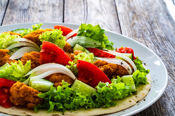 Seared chicken nuggets with vegetable salad on tortilla on wooden background
