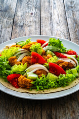 Seared chicken nuggets with vegetable salad on tortilla on wooden background
