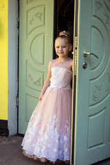 Welcome. A beautiful girl, dressed in a cute dress, is friendly standing by the open door.