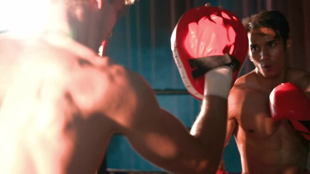 Asian and Caucasian Muay Thai boxer unleash punch in fierce boxing training session, delivering punching strike to sparring trainer, showcasing Muay Thai boxing technique and skill. Impetus