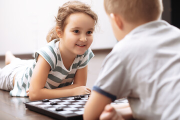 Teenager boy and little girl play chess at home