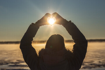 Woman making heart with hands outdoors in a frosty sunset, closeup. Winter solstice. High quality photo
