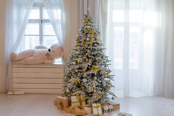 Snow-covered Christmas tree with gifts and toys in the interior of a room with windows