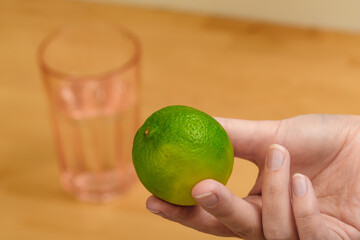 Zielona limonka trzymana w dłoni, w tle szklanka z wodą - obrazy, fototapety, plakaty