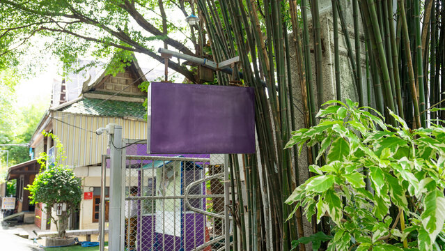 Picture of the sign hanging in front of the temple gate. On the side, a bamboo arch was planted to surround the fence. And there is a clump of shrubs planted at the front. At the back is a traditional
