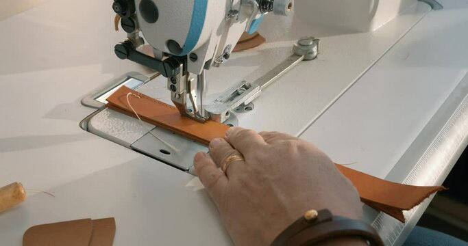 male craftsman stitches a men's leather belt on a sewing machine Close up shot slow motion