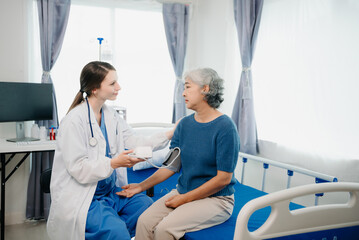 Obraz premium Doctor in white suit take notes while discussing and Asian elderly, woman patient who lying on bed with receiving saline solution in hospital or clinic.