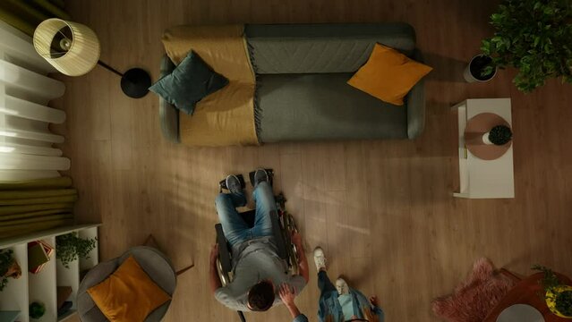 Top view shot of a couple with disabilities spending time together. A man on a wheelchair helps a sight impaired woman sit on the couch. They hold hands and talk.