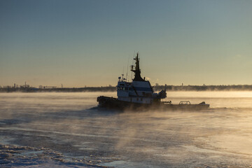 The tugboat breaks the ice near the shore in a foggy frozen river. High quality photo