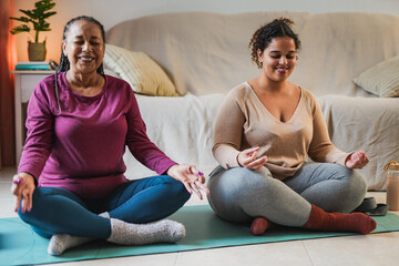 Happy african mother and adult daughter doing yoga meditiation at home during winter time - obrazy, fototapety, plakaty