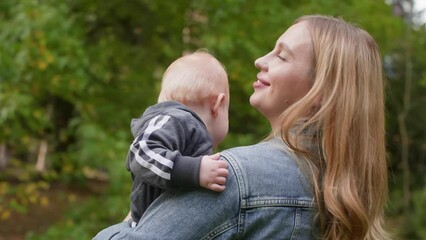 Loving caring blonde mom holding happy baby son boy walking in autumn park. Young mother enjoying motherhood parenting outdoors on nature. Maternity leave, baby care, babyhood, raising boy concept.