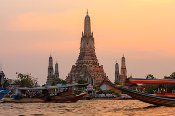 Obraz premium Wat Arun Ratchawararam Ratchawaramahawihan at sunset time The foreground is the Chao Phraya River. There are tour boats passing by. It is a recommended tourist attraction in Bangkok, Thailand.