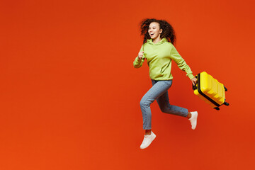 Fototapeta na wymiar Side view traveler excited woman wear casual clothes run hold suitcase bag isolated on plain orange background. Tourist travel abroad in free spare time rest getaway. Air flight trip journey concept.