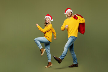 Full body side view merry young couple two friends man woman wear sweater Santa hat posing hold...