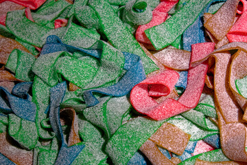 A close-up of colorful sour gummy candy in the shape of belts or ribbons, covered in sugar crystals.