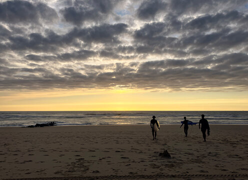 A group of surfers on their way to the Atlantic Ocean with the setting sun in front of them