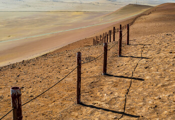 Stunning desert view in Paracas National Reserve with rusty metal fence delimiting the protected area, Peru 
