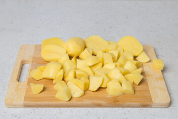 Potatoes cut into cubes for cooking are prepared on a wooden cutting board.
