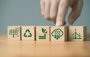 Hand pushing carbon reduction icon on wooden block cube among environmental ecology icon include...