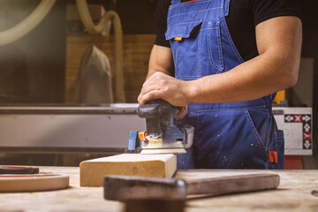 Close up of an young man builder carpenter equals polishes wooden board with a  random orbit sander...