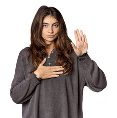 Young Caucasian woman in studio setting taking an oath, putting hand on chest.